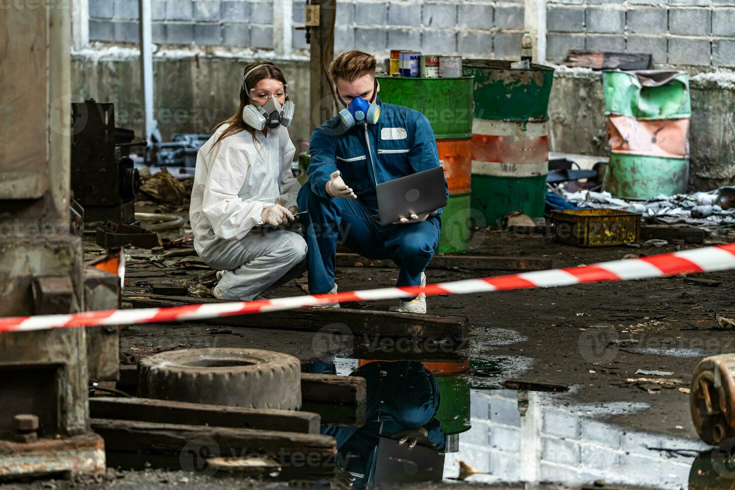 emergency pollution factory concept. engineers wearing mechanic jumpsuits and ppe and gas masks inspect oil on the factory floor. photo