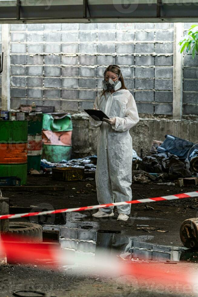 emergency pollution factory concept. Female chemist wearing PPE and gas mask inspecting oil on factory floor photo