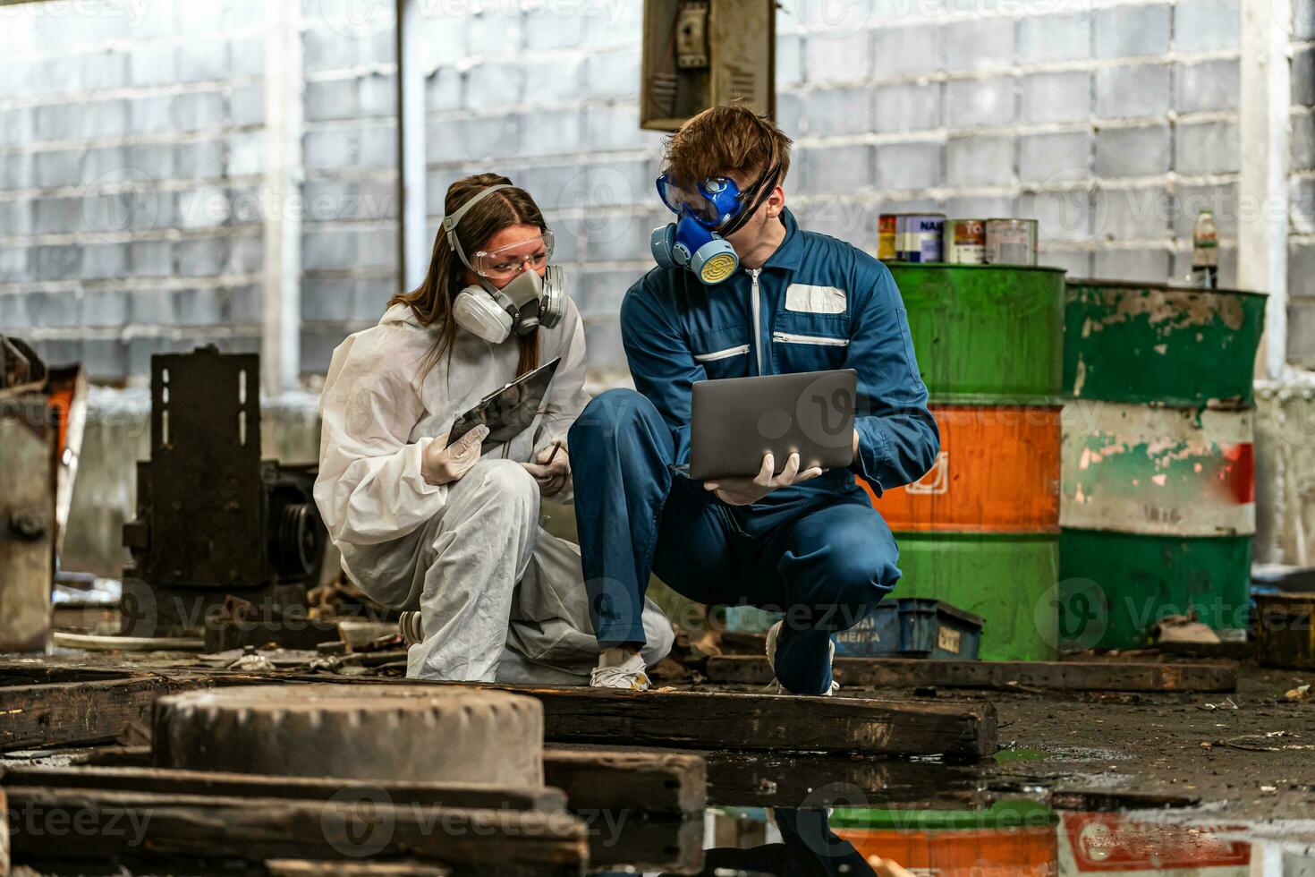 emergency pollution factory concept. engineers wearing mechanic jumpsuits and ppe and gas masks inspect oil on the factory floor. photo