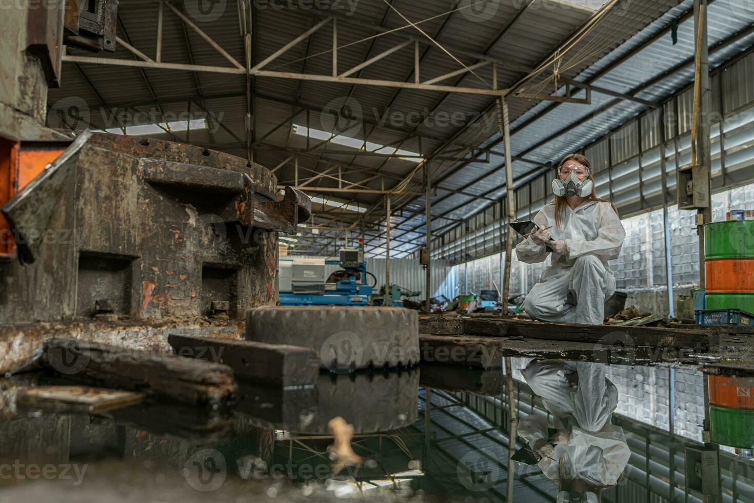 emergency pollution factory concept. Female chemist wearing PPE and gas mask inspecting oil on factory floor photo