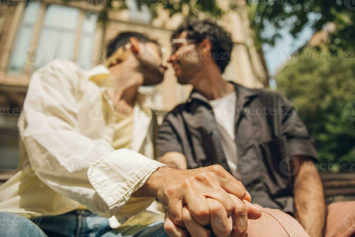 men sitting on a bench in the city kissing ang huging each other photo