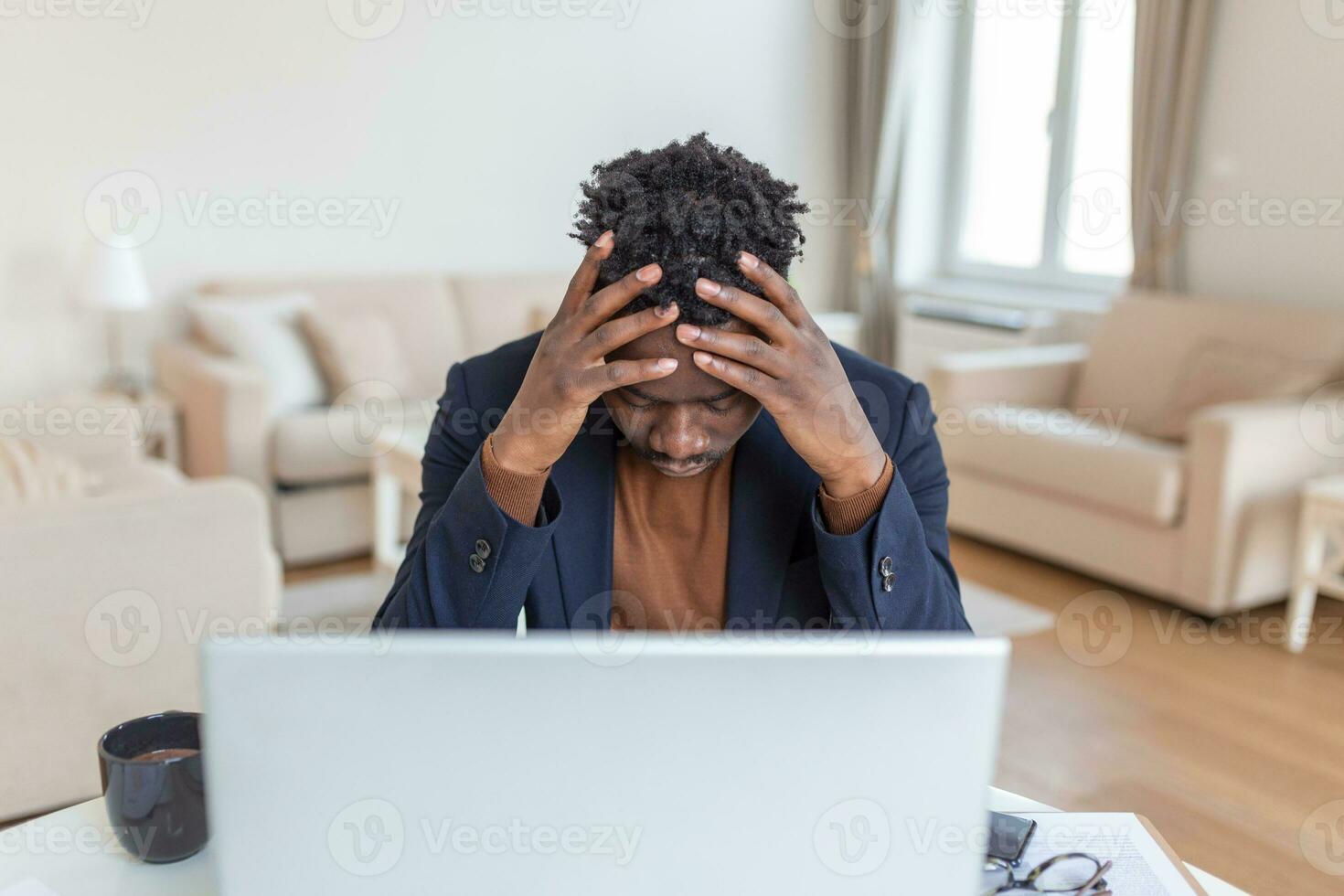Stressed-out young businessman sitting with his head in his hands while working at a desk in an office. Portrait of frustrated young man with laptop working indoors, home office concept. photo