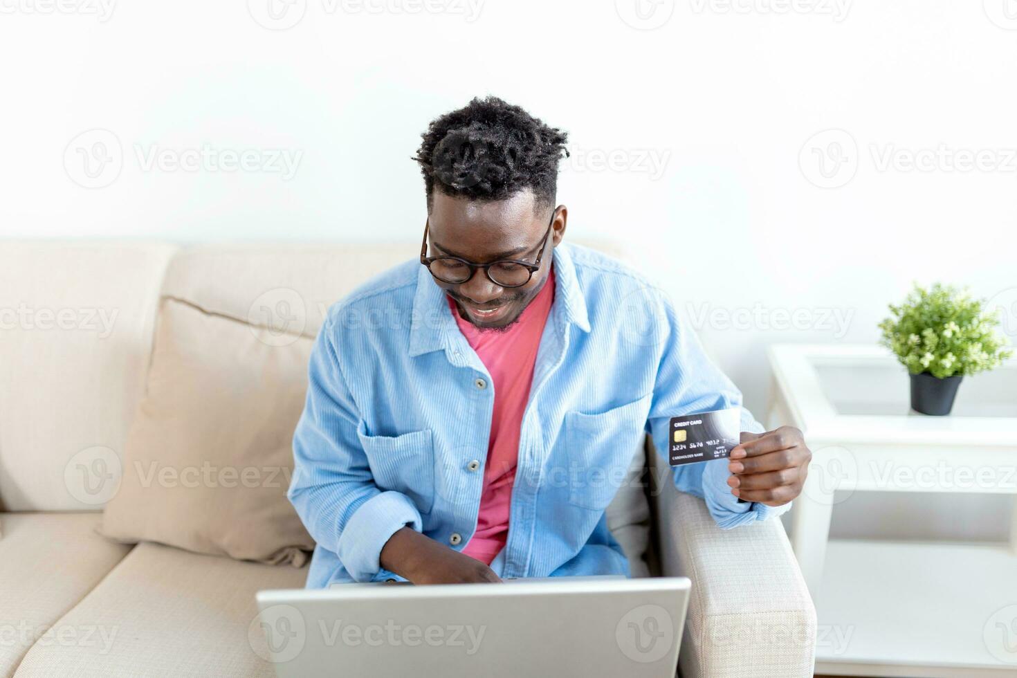 Internet payment. Happy cheerful man looking at the laptop screen while making an Internet payment. Happy young man with credit card and laptop sitting on sofa at home. Online payment photo