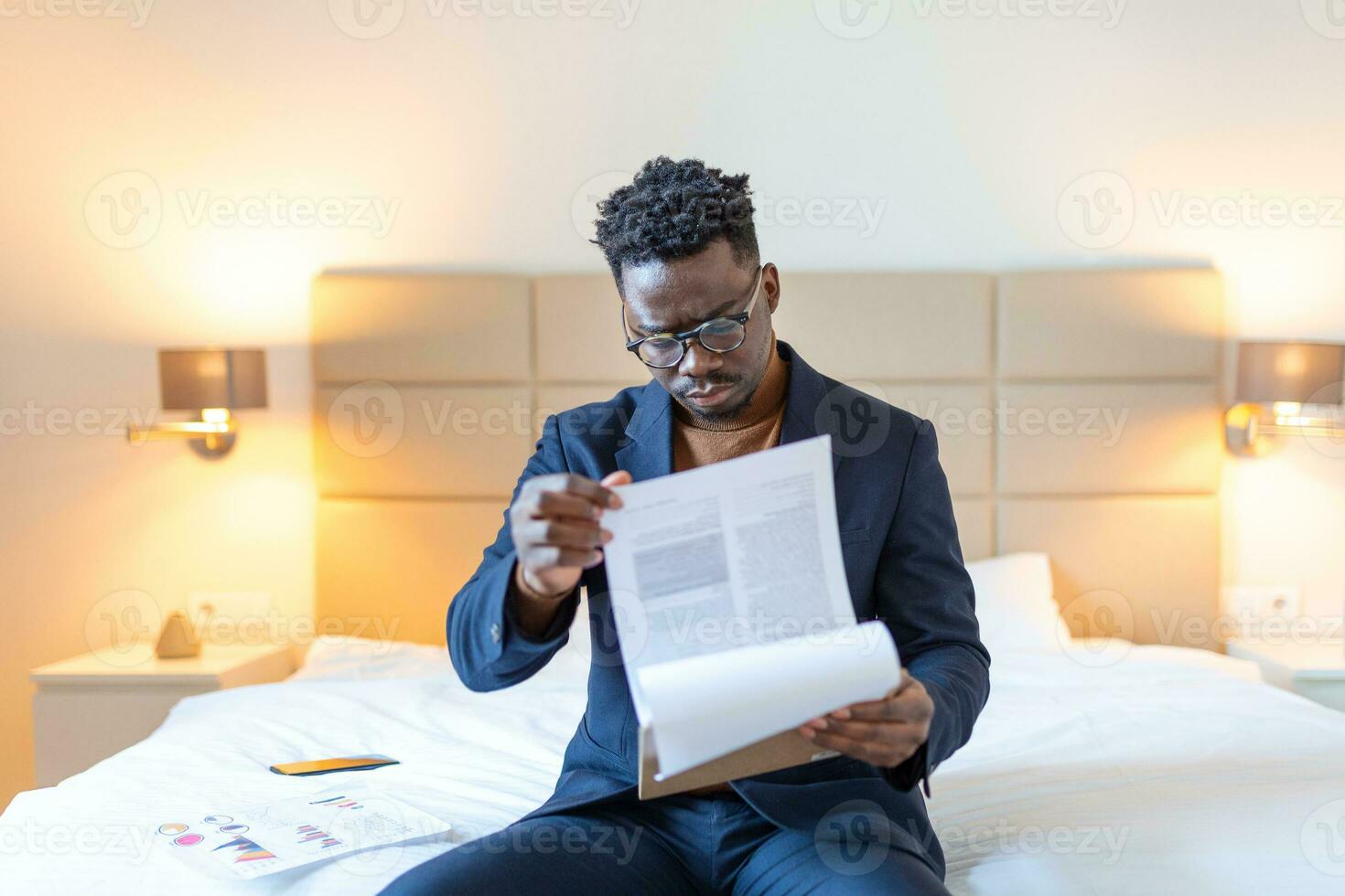 Serious Arican business man sitting on hotel bed working, analyzes expenses on business trip at the hotel room. photo