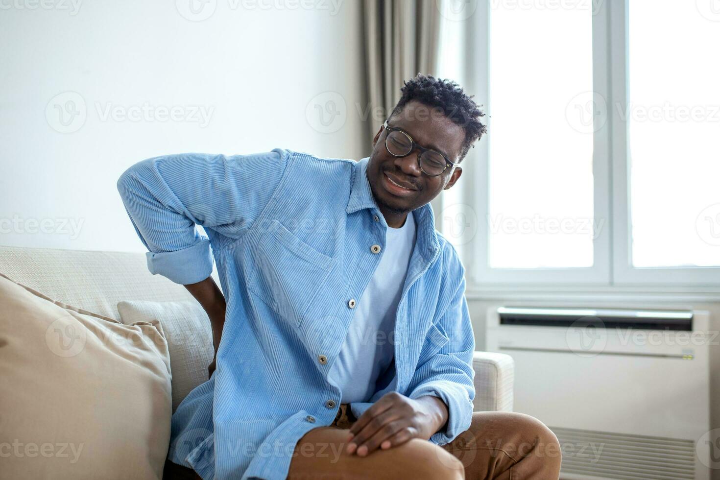 unhappy Man suffering from backache at home. Lower Back Pain . Man feels back pain massaging aching muscles, sad man suffers from low-back photo