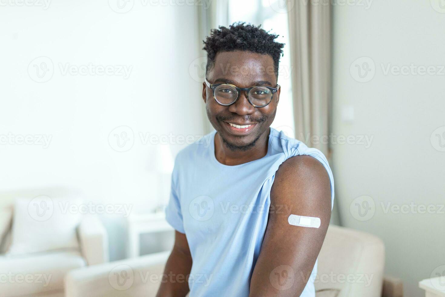 Portrait of a man smiling after getting a vaccine. African man holding down his shirt sleeve and showing his arm with bandage after receiving vaccination. photo
