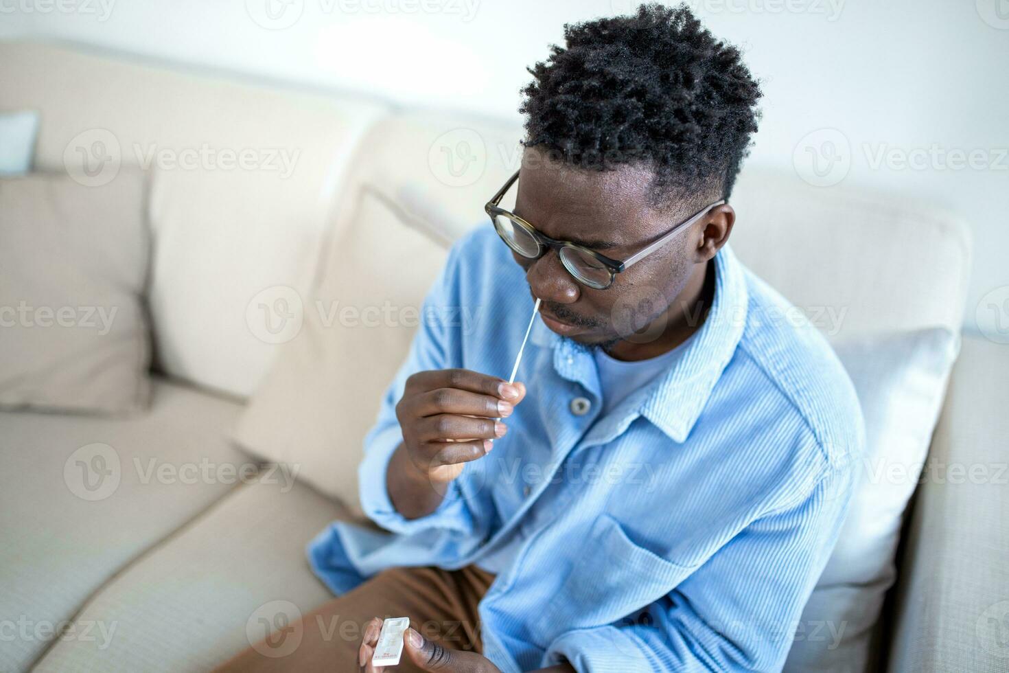 Shot of a African man using cotton swab while doing coronavirus PCR test at home. man using coronavirus rapid diagnostic test. Young man at home using a nasal swab for COVID-19. photo