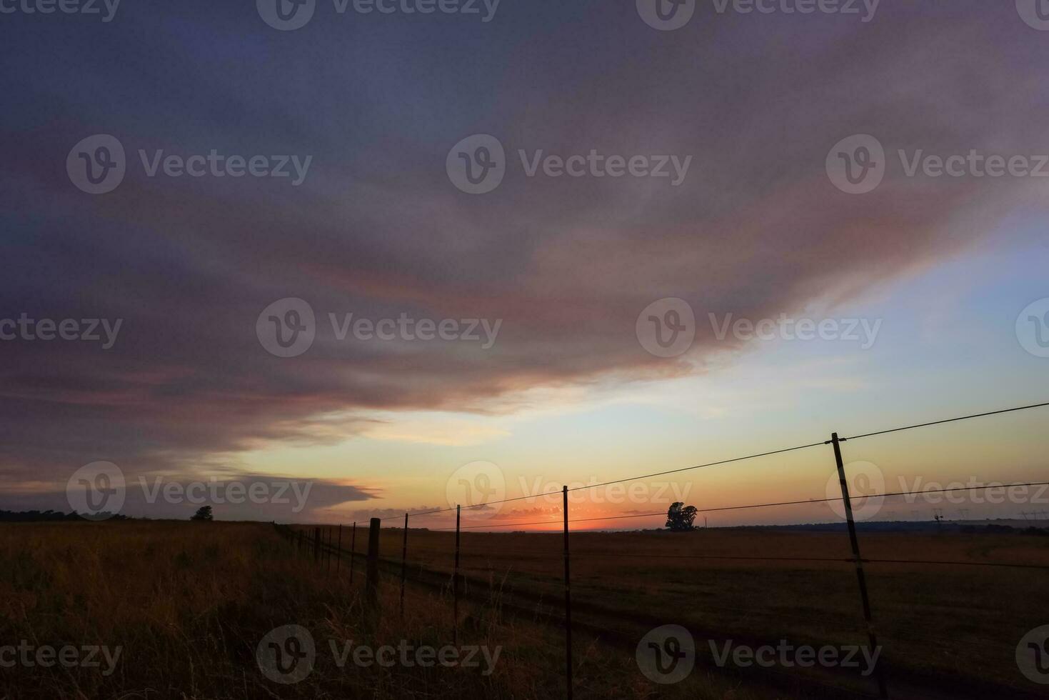 a sunset over a field with a fence and a fence post photo