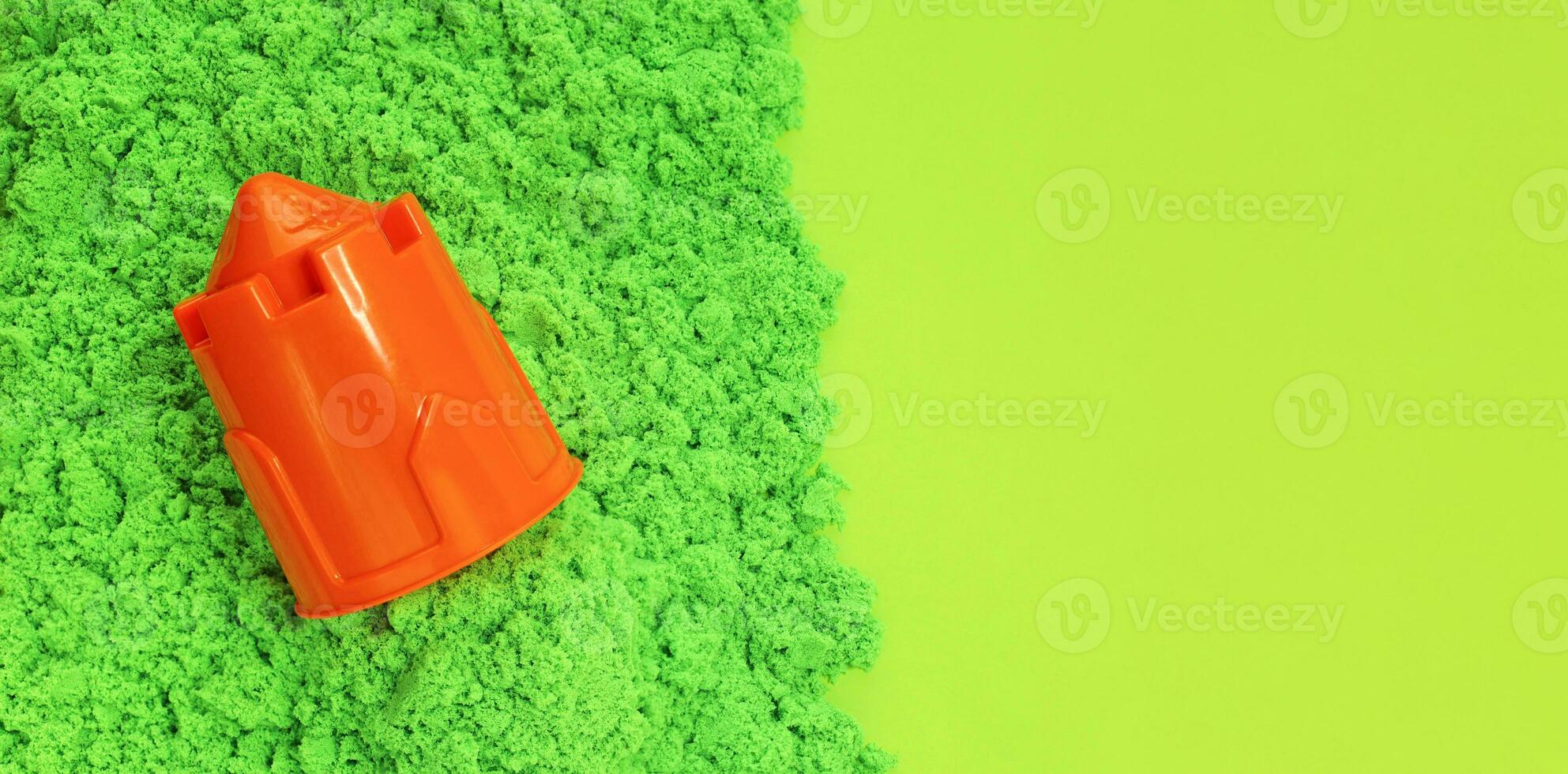 Green kinetic sand with orange plastic sand mold in form of castle tower. Kids sensory game, modeling of colored sand. Light green paper background with copy space, long banner. photo