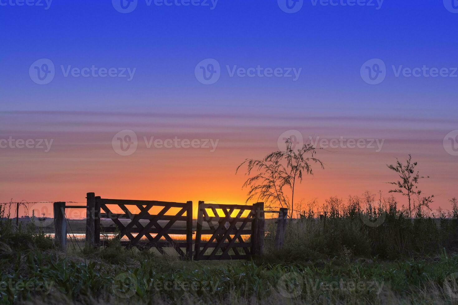a sunset over a field with a gate photo