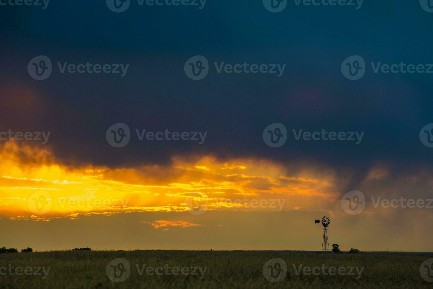 un molino en un campo con un puesta de sol detrás eso foto