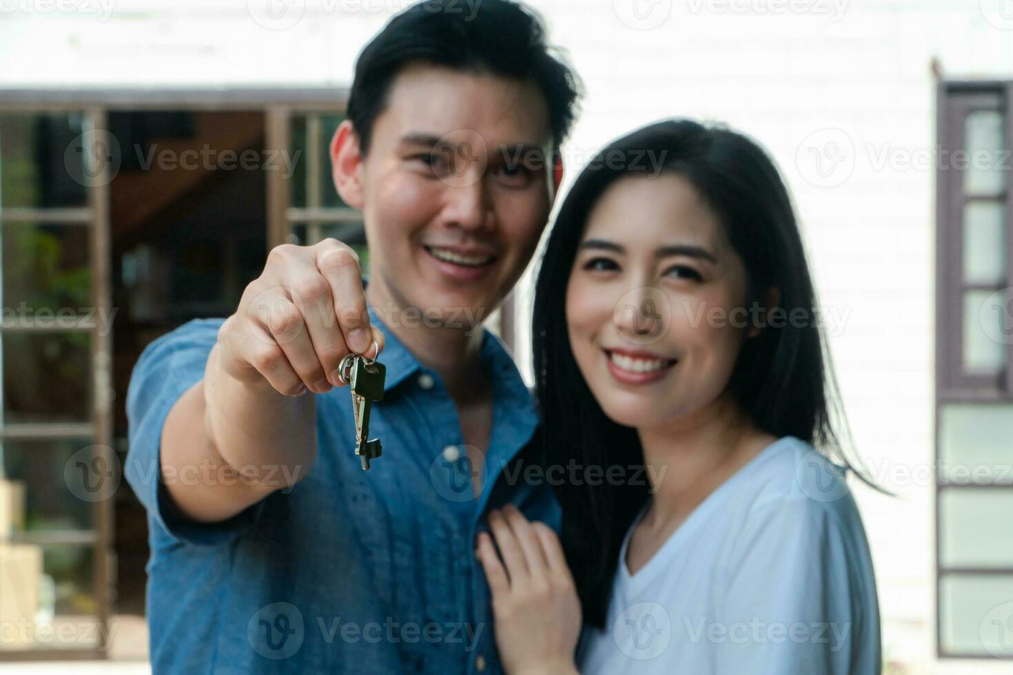 feliz pareja sonriente frente a la casa y sosteniendo las llaves de la nueva casa el día de la mudanza, y comenzar una nueva vida familiar. concepto de propietario y reubicación foto