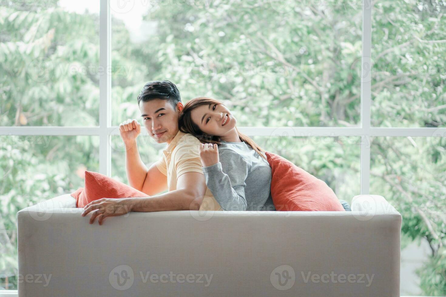 una pareja feliz sentada en el sofá y siendo un hombre se burla de su novia con amor en la sala de estar y se relaja. concepto de romántico en el día de san valentín. propuesta y matrimonio foto