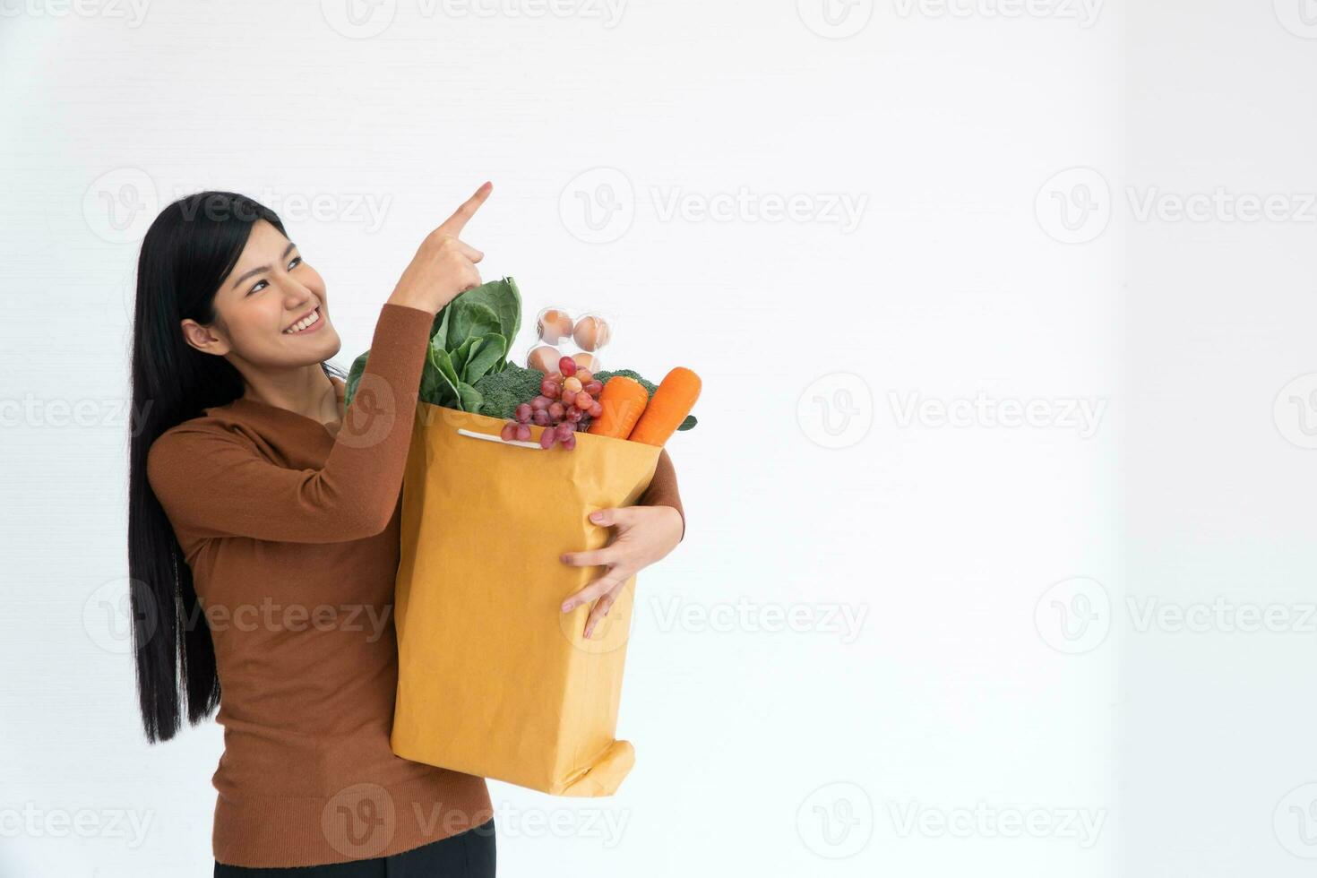 Happy Asian woman is smiling and finger up and carries a shopping paper bag after the courier from the grocery came to deliver his goods at home. Concept of Supermarket delivery for a new lifestyle photo