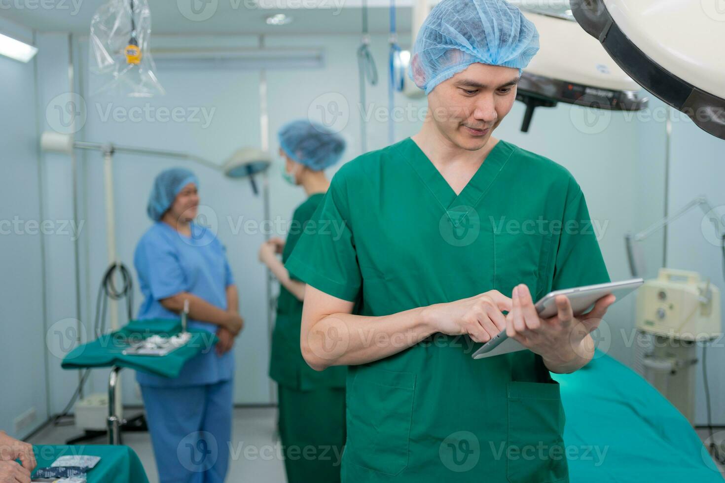 Portrait of Asian surgeon with medical mask standing and holding a tablet in operation theater at a hospital. Team of Professional surgeons. Healthcare, emergency medical service concept photo