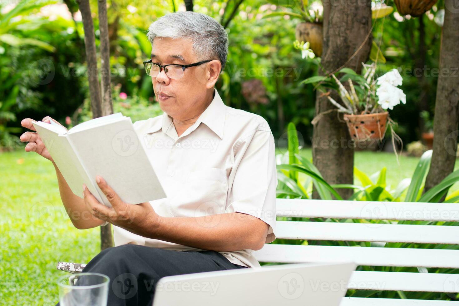 senior old man reading a book in the park and drinking water. Concept of retirement lifestyle and hobby. photo