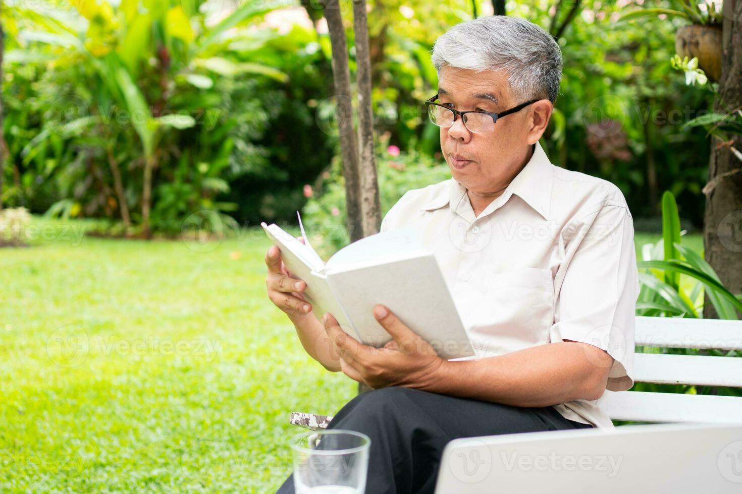 senior old man reading a book in the park and drinking water. Concept of retirement lifestyle and hobby. photo