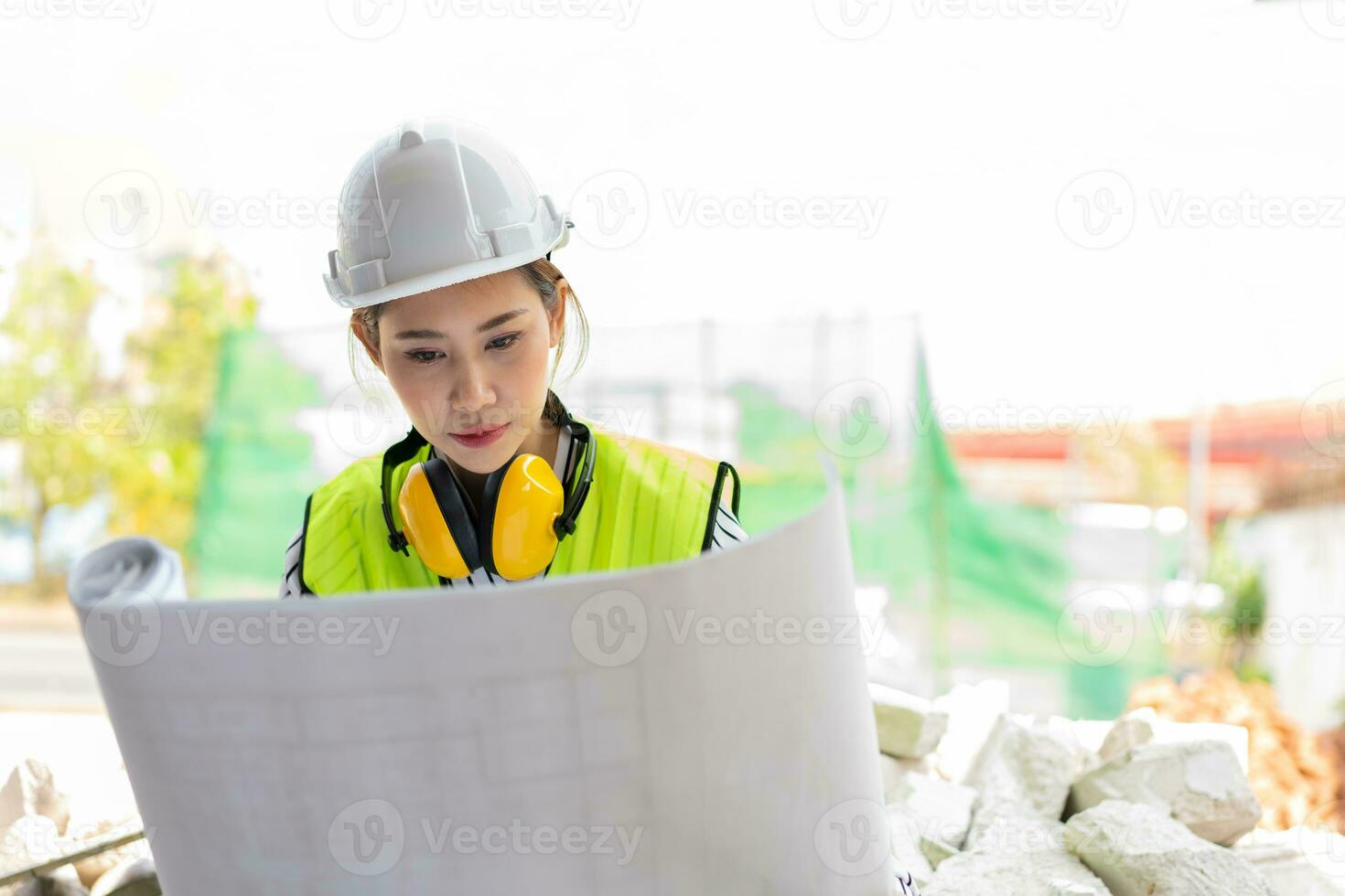 Asian engineer or Young woman Architect put on a helmet for safety and look at Blueprint for Inspect Building factory Construction Site on a construction site. Smart working woman concept. photo