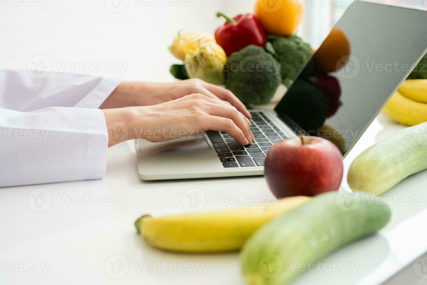 retrato de una nutricionista asiática sonriente escribiendo en una computadora portátil para un plan de dieta correctiva equilibrada para pacientes o consejos para perder peso. concepto de estilo de vida saludable, comida saludable, dieta foto