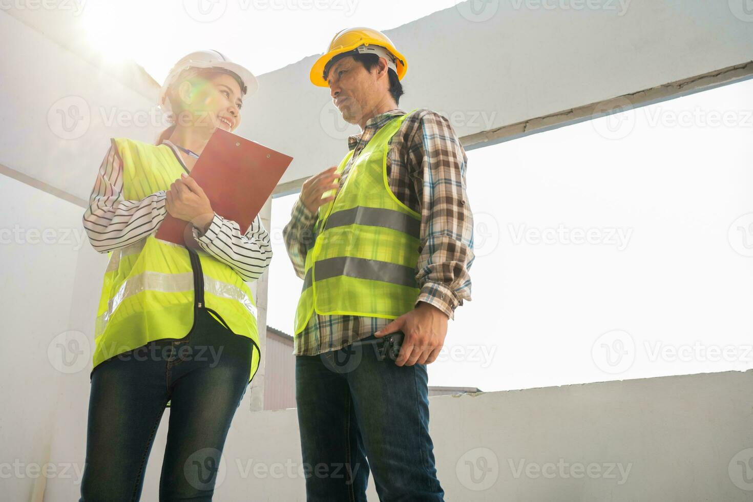 Asian engineer or Young Female Architect put on a helmet for safety and talk with a contractor on a construction building factory project, Concept of Teamwork, Leadership concept. photo