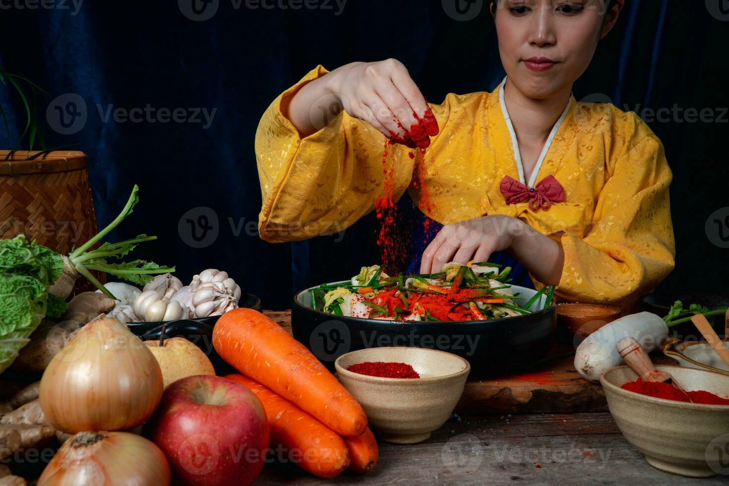 Asian women wearing Korean traditional costumes hanbok are mixing fresh stir-fry and kimchi ingredients with ingredients such as salt, garlic, gochugaru, fresh vegetables. photo