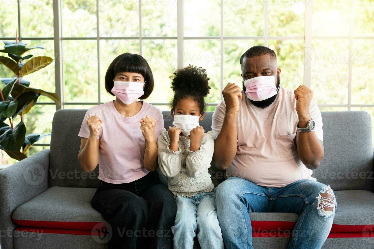 Mixed Race family sitting on the sofa and wearing medical face masks for against coronavirus world pandemic and stay quarantined together at home social distancing new normal lifestyle photo