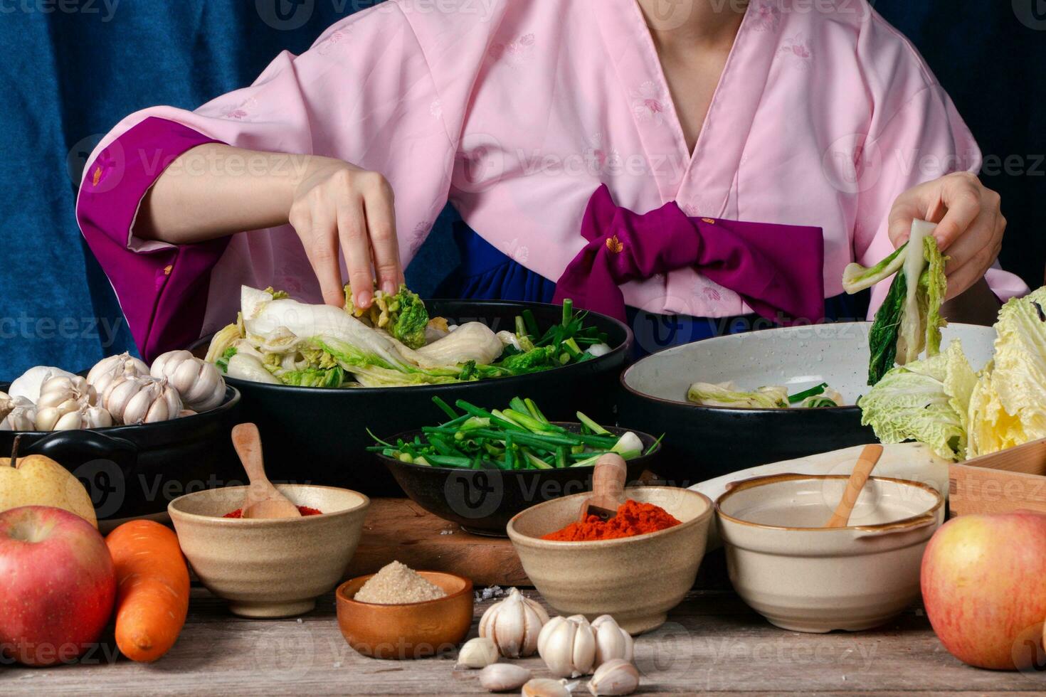 Asian women wearing Korean traditional costumes hanbok are mixing fresh stir-fry and kimchi ingredients with ingredients such as salt, garlic, gochugaru, fresh vegetables. photo