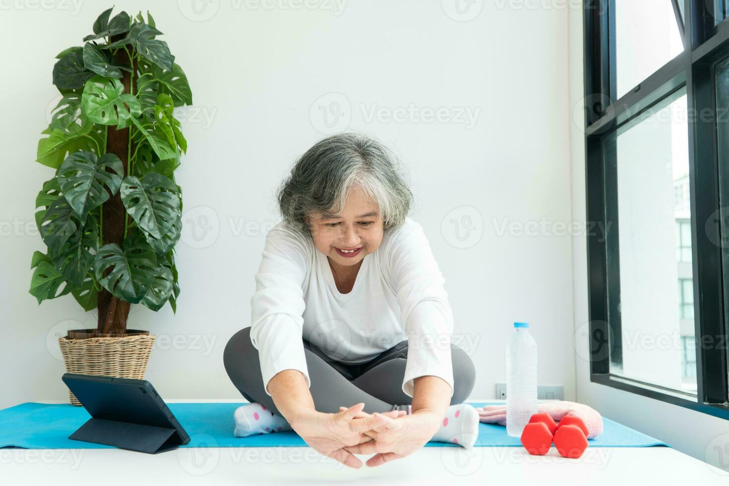 anciana asiática viendo cursos en línea en una computadora portátil mientras hace ejercicio en la sala de estar en casa. concepto de entrenamiento en línea. foto