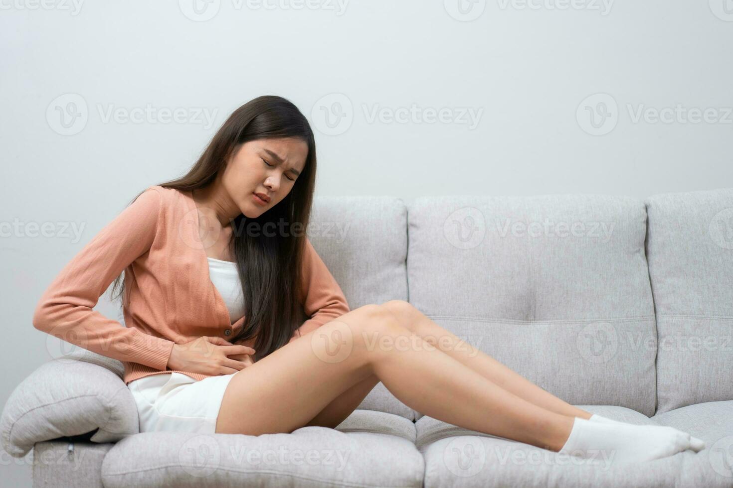 Sick Asian Woman Suffering From Acute Abdominal Pain in the abdomen due to menstruation period, PMS.  Sitting On Couch, stomachache from food poisoning, abdominal pain, digestive problem, gastritis photo