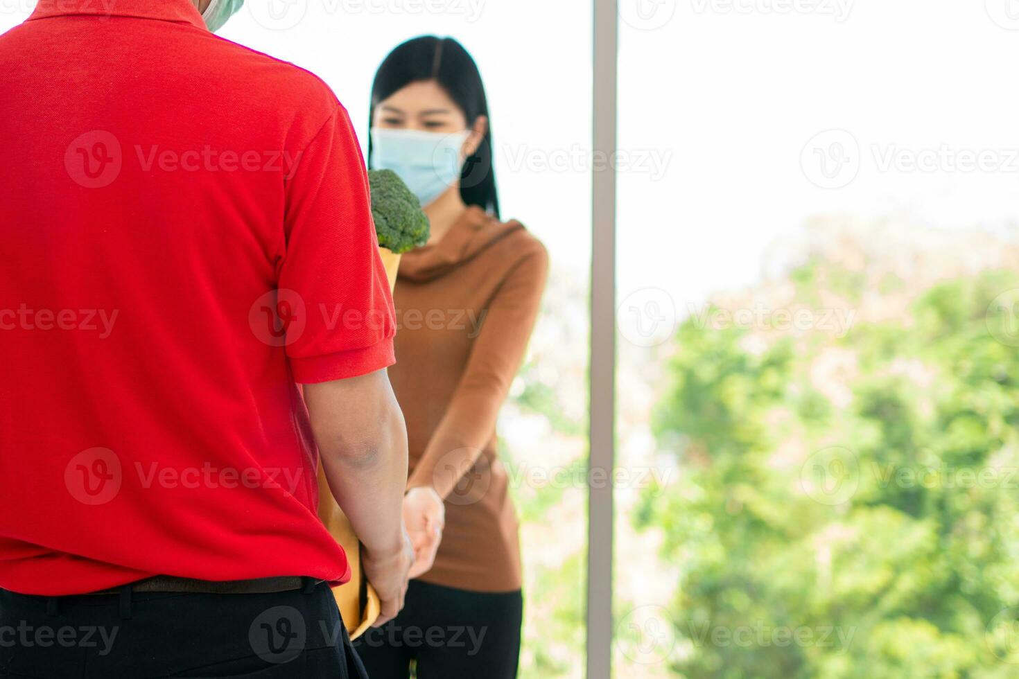 asiático mujer vistiendo un cara máscara y recoger compras bolso de Fresco alimento, verduras, y frutas desde un entrega hombre desde un supermercado. concepto de Rápido tienda de comestibles Servicio y nuevo estilo de vida foto