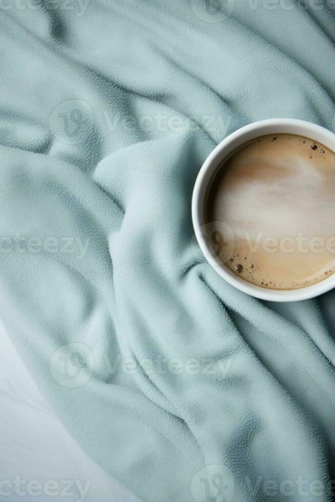 A coffee cup is placed on top of a grey blanket photo