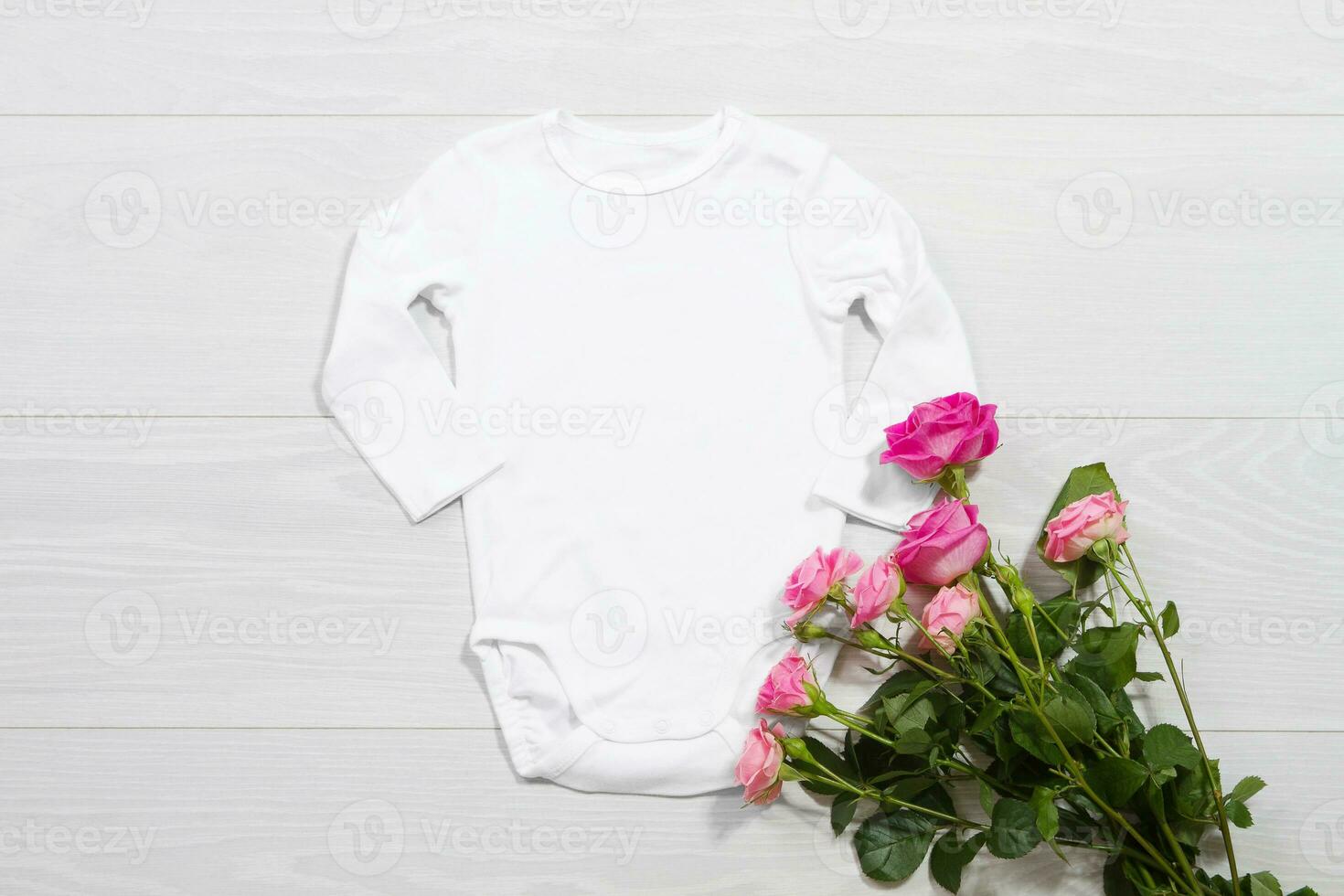 White mockup newborn shirt. Wooden background, pink roses, happy birthday. Blank template jumpsuit bodysuit front top view. Baby clothing. Bouquet of flowers photo