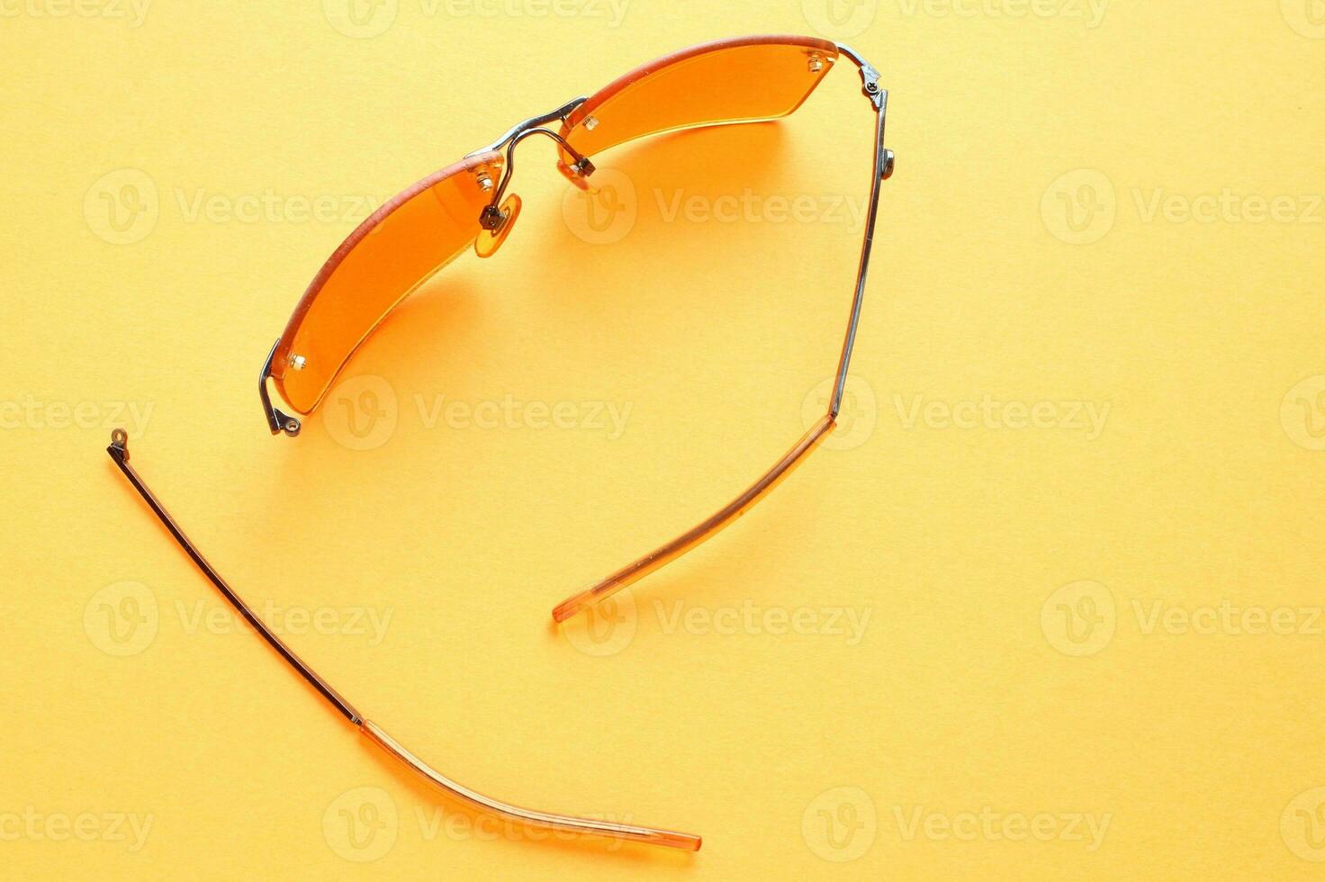 Old broken eyeglasses with damaged legs on yellow background. Poor eyesight. Reuse and repair concept. Idea of health. Failure optic eyewear. Breakage of vision correction glasses. Close up, flat lay photo
