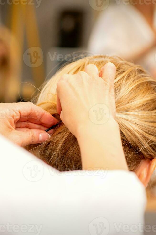 Hair stylist's hands doing professional hairstyling of female long hair in a beauty salon. photo