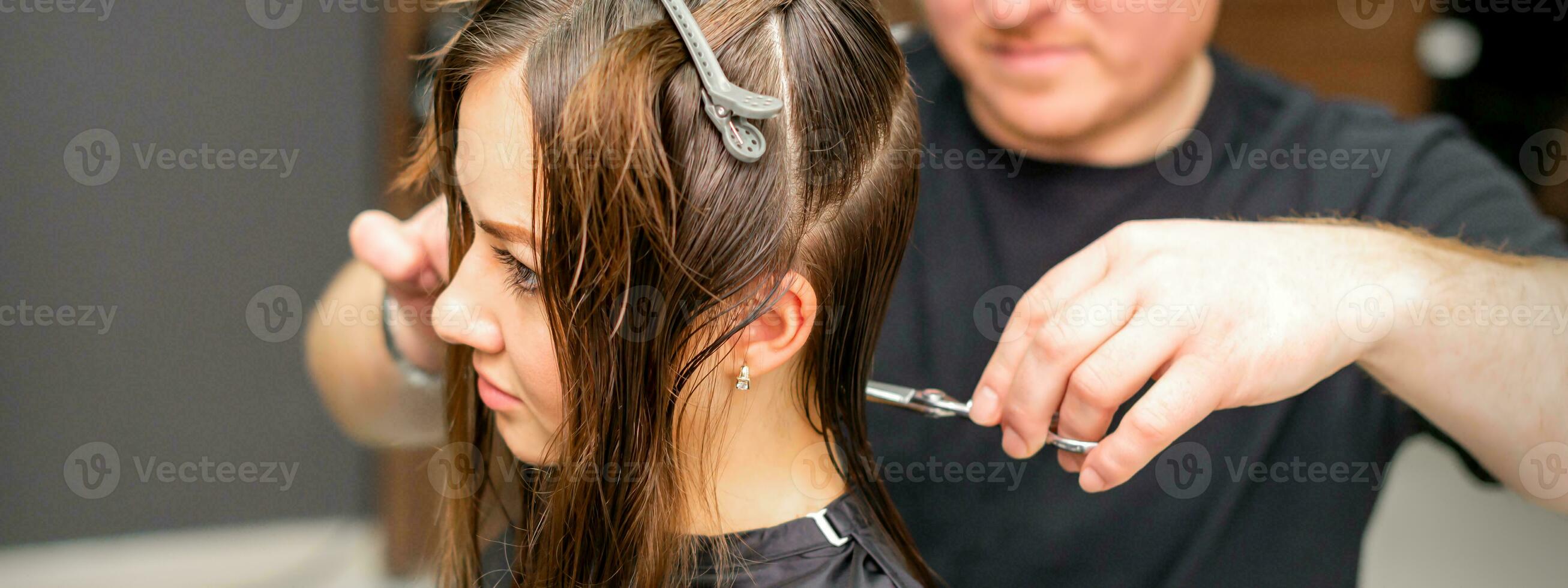 Male stylist cutting the hair of female client in professional beauty salon. photo