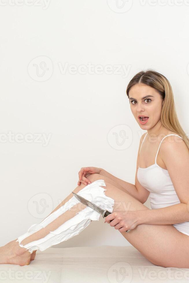 Beautiful caucasian woman shaving her legs with a knife with shaving foam on white background. Depilation and epilation concept. photo