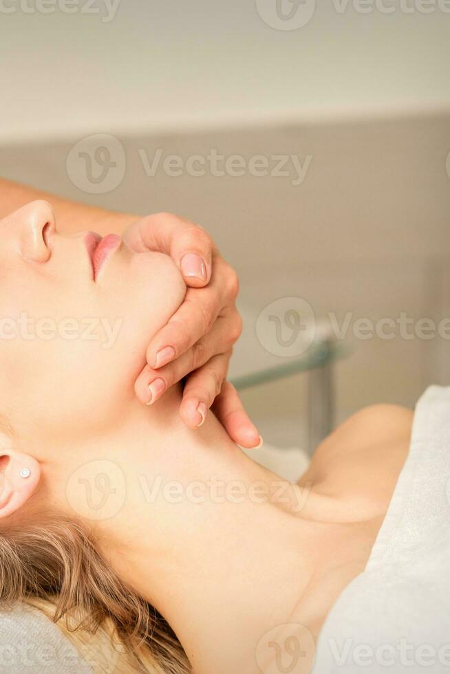 cosmetóloga manos haciendo facial masaje en frente y barbilla de joven hembra a spa salón. foto