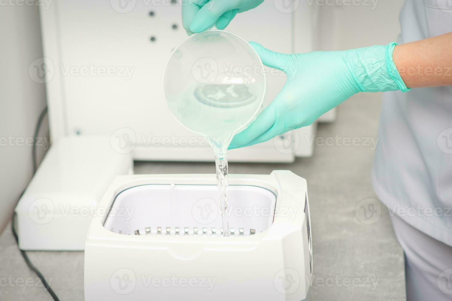 The beautician adds liquid for disinfection of instruments to the machine for sterilization of tools. photo
