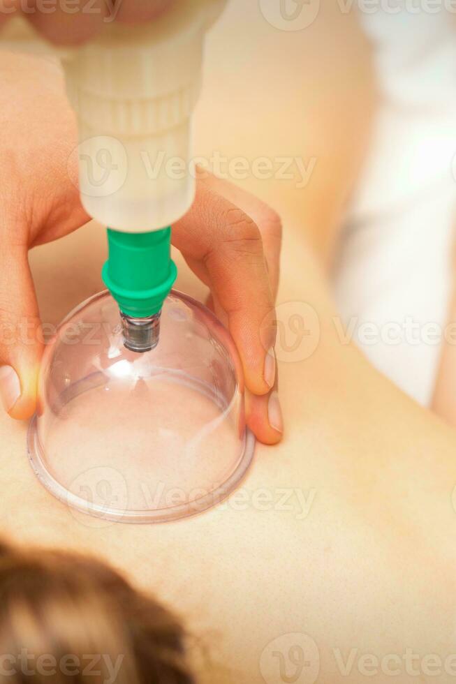 Woman receiving vacuum cupping treatment on back laying on the chest in massage salon. photo