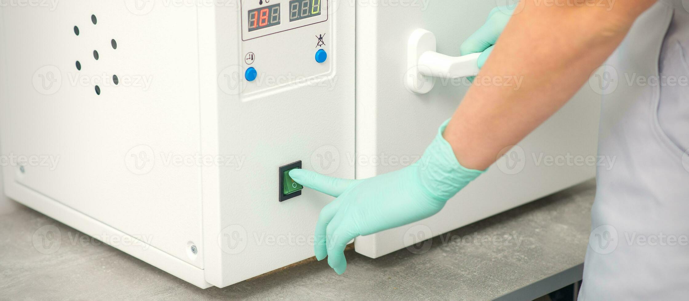 Beautician in protective gloves starts the machine for disinfection of tools before the depilation procedure. photo