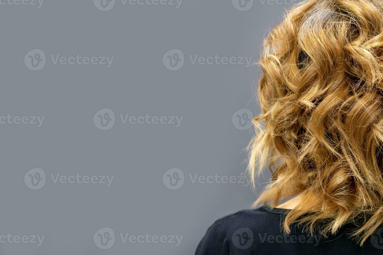 Back view of the woman with long brown curly hair stands on a dark background. photo