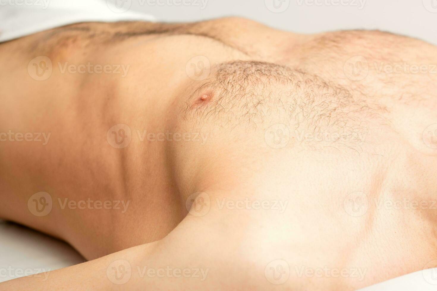 Hairy body, stomach, and chest of a man lying before epilation. photo