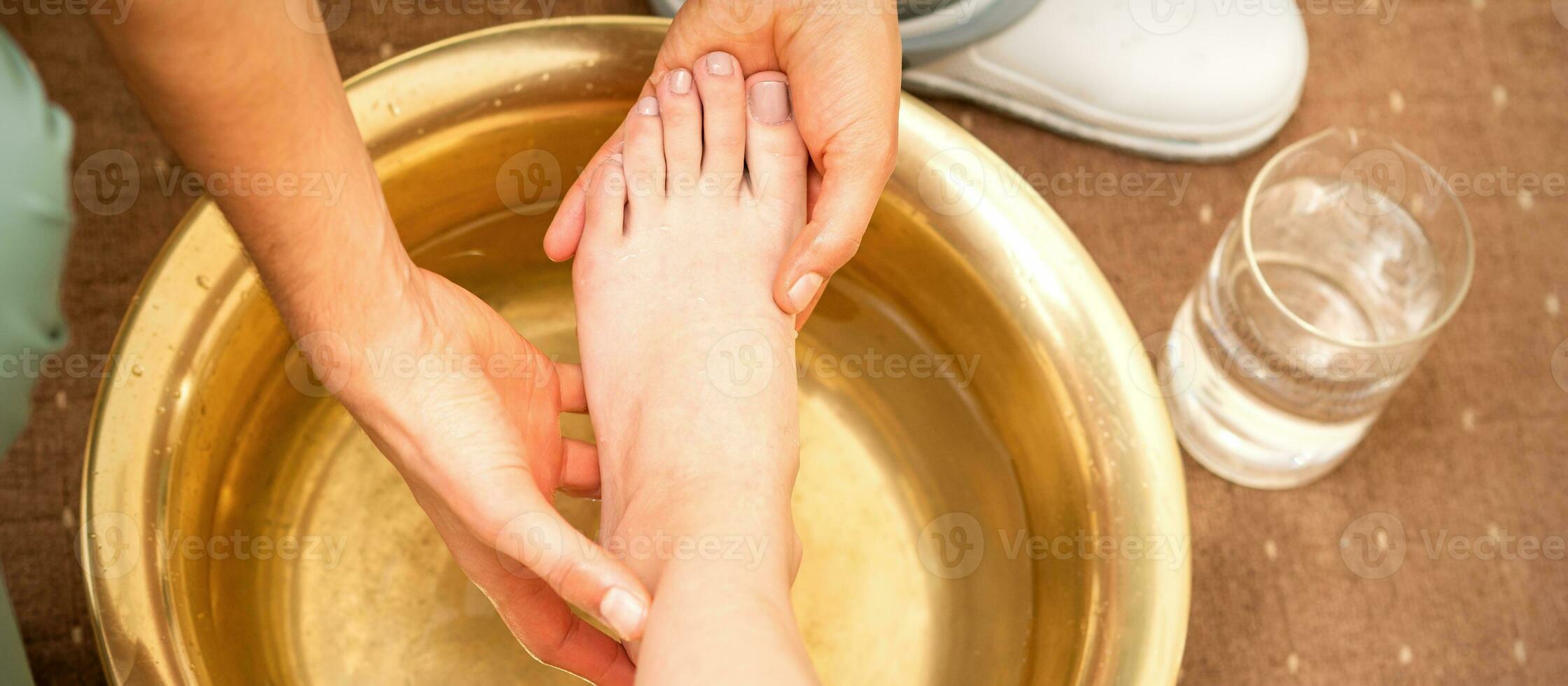 Washing female foot in a special container by male masseur in spa salon. photo