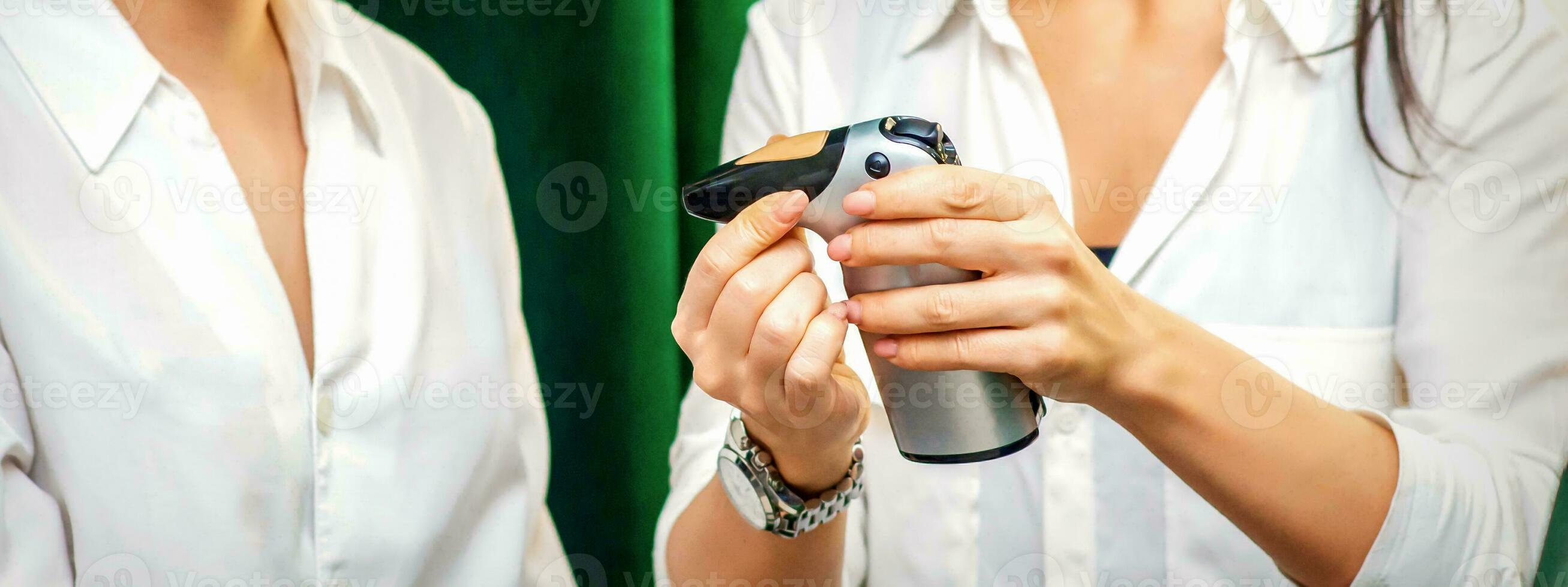 Smiling makeup artist shows for her smiling client aerograph tool device before airbrush procedure in a beauty salon. photo