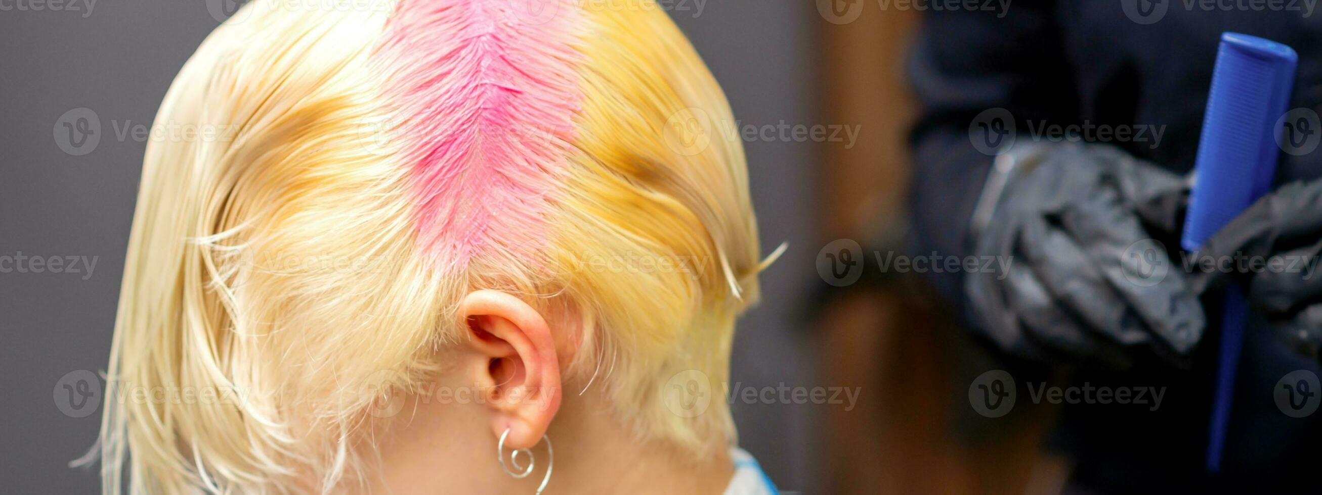 Young caucasian woman tints hair roots in pink color in a beauty salon. photo