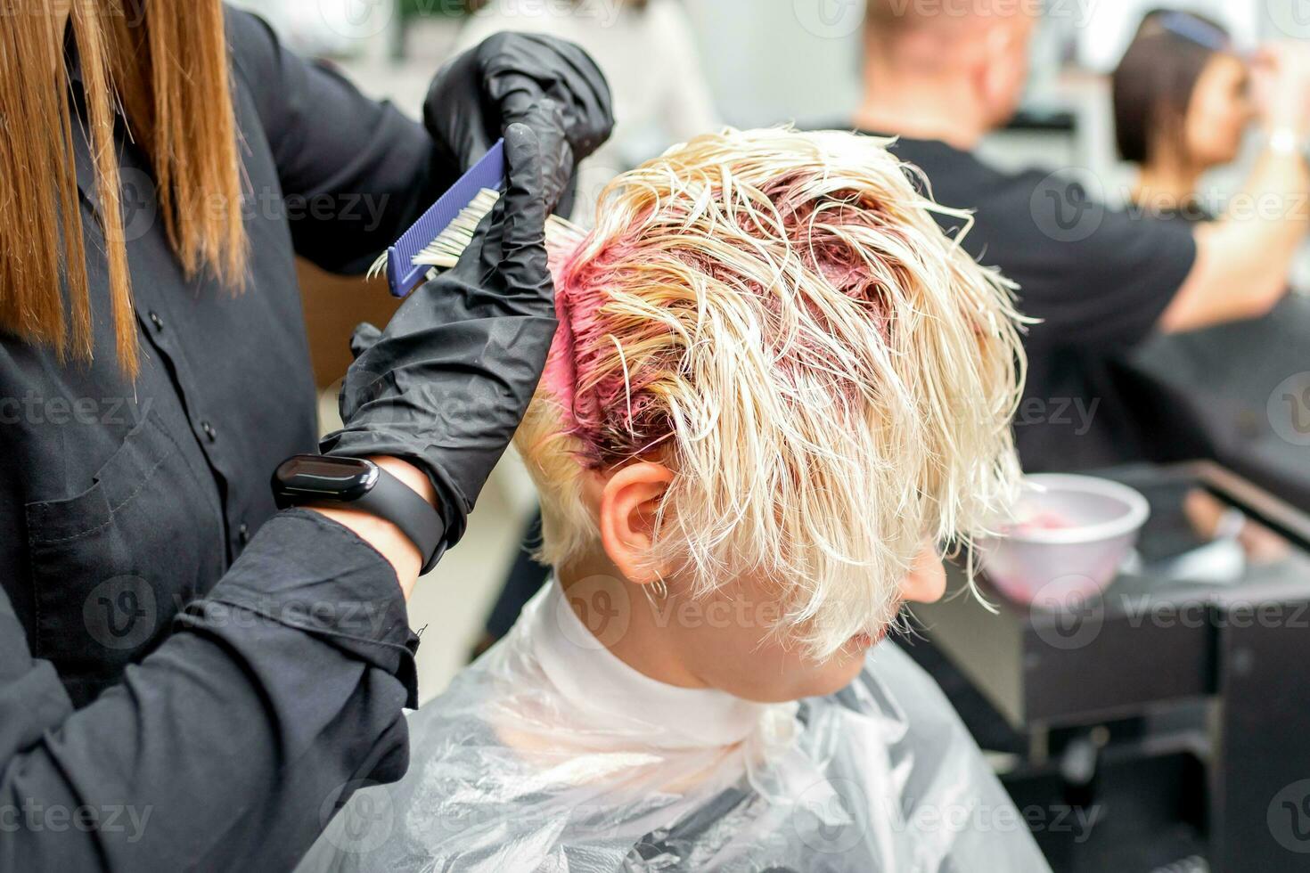 el profesional peluquero usos un cepillo a aplicar el rosado colorante a el cabello. pelo colorante concepto. foto