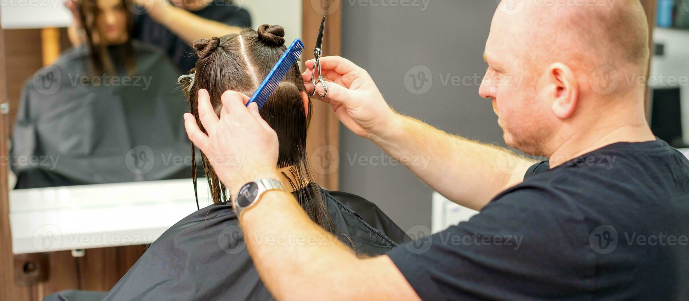 Male stylist cutting the hair of female client in professional beauty salon. photo