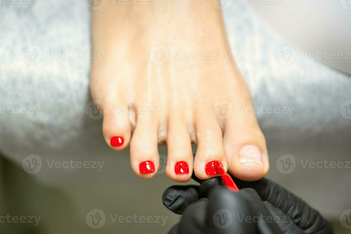 pedicuro aplicando rojo uña polaco a el hembra uñas de los pies en un belleza salón. foto