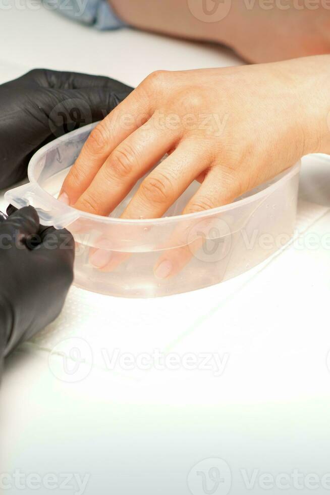 el hembra sumergido su mano en un cuenco de agua reblandecimiento uñas preparando para el manicura. foto