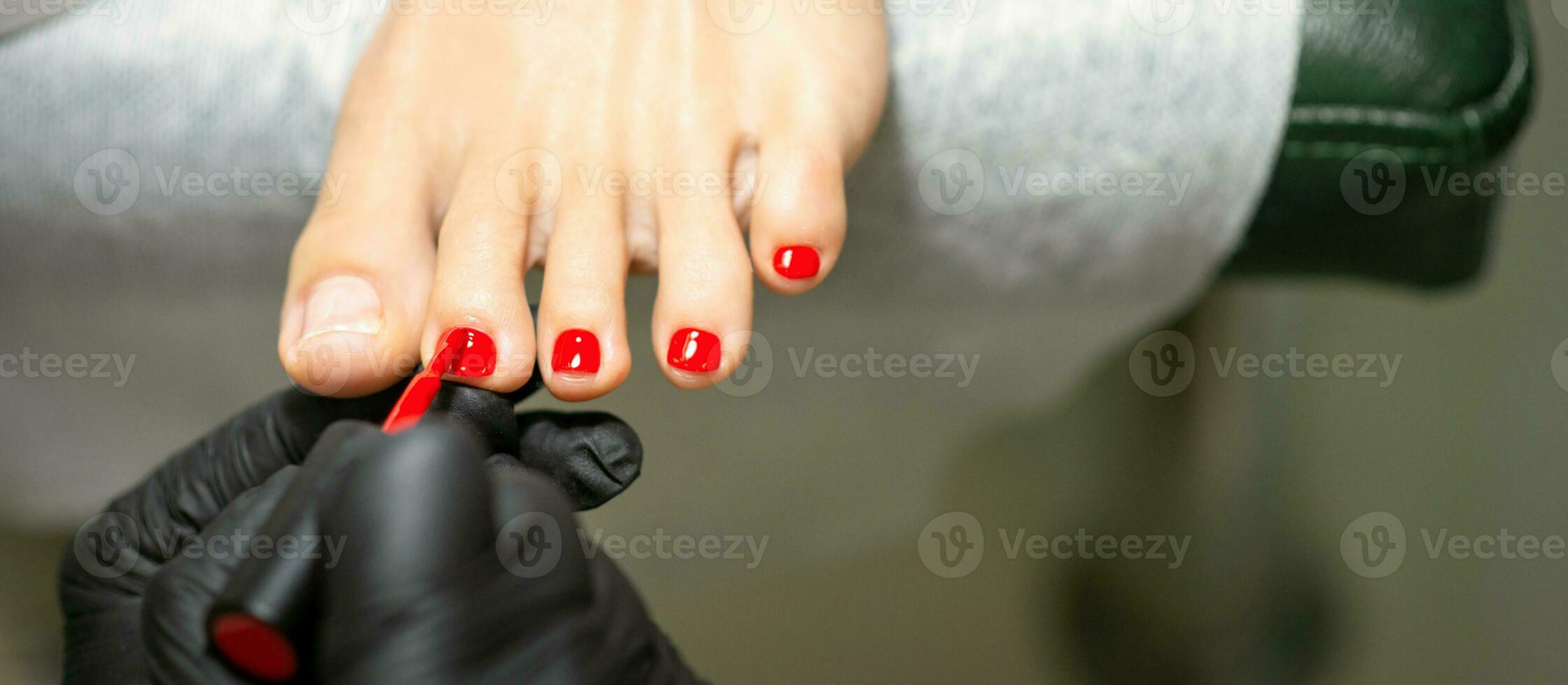 pedicuro aplicando rojo uña polaco a el hembra uñas de los pies en un belleza salón. foto